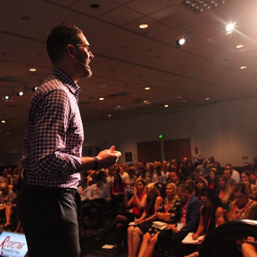 Greg McDaniel speaking on stage at a real estate industry conference